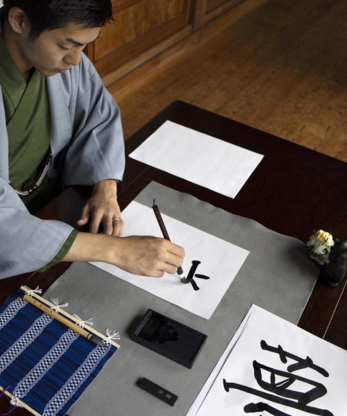 man-practicing-japanese-handwriting-with-assortment-tools